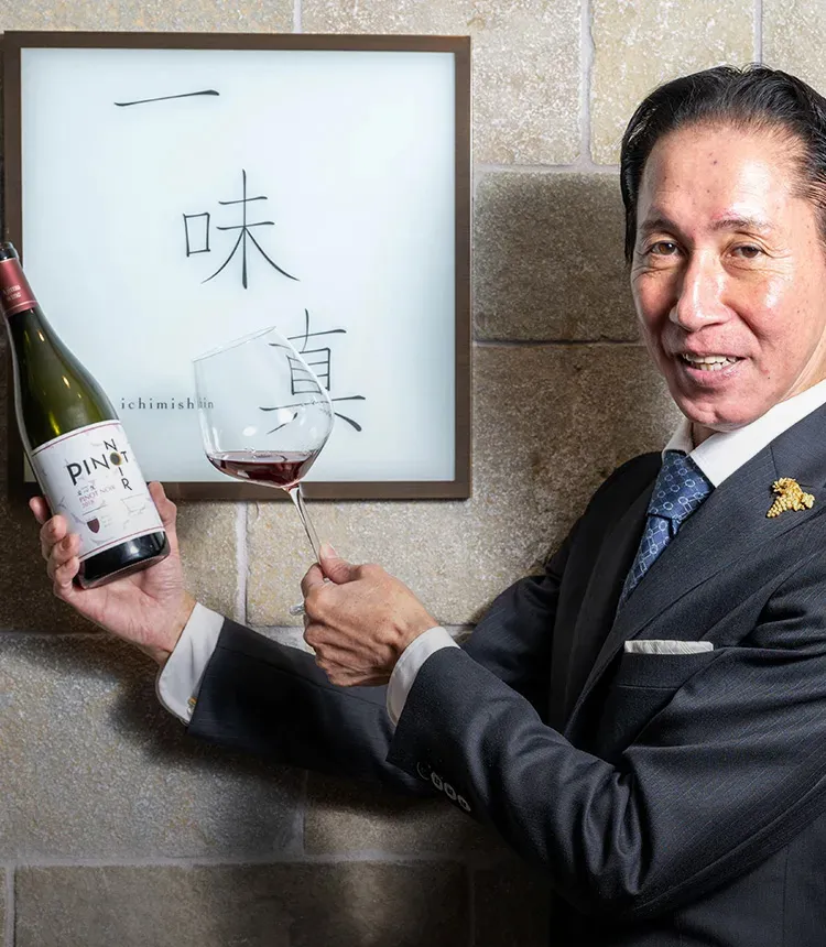 「一味真」の店前で。手にするのは「安心院（あじむ）ワイン ピノ・ノワール」