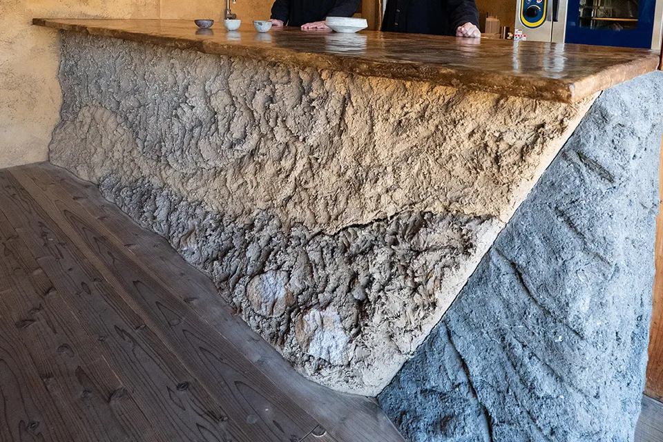 向かいの山の土を使ったカウンターの壁面は、土を掘った時に見えた地層の色の違いを再現し、出てきた石を配した。左官の江口さんからは「地層があって、大地がある。その大地の上で料理をしてください」と言葉を贈られたそう